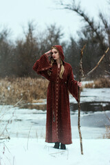 Bright color photo of a beautiful sorcerer girl with blond braids in a winter forest next to a...