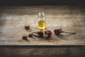 Essential oil in a small glass bottle with dried pink roses in bud on a wood background