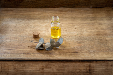 Obraz na płótnie Canvas Essential oil in a small glass bottle with eucalyptus sprigs on a wood background