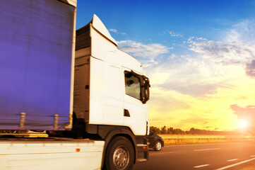 Close-up of a big truck with a trailer on a countryside road against a sky with a sunset - 546998111