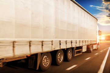 Close-up of a big truck with a trailer on a road in motion against a sky with a sunset - 546998120