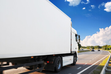 Close-up of the big truck with a trailer on a countryside road against a sky with clouds - 546998143