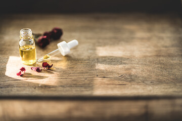 Essential oil in a small glass bottle with dried pink roses in bud on a wood background