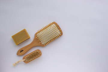 Beauty accessories wooden comb, nail brush, soap bar on white background. Modern paddle hair brush on table. Top view, flat lay, copy space.	
