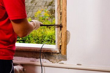 The man with a hand saw cuts the mounting wool around the window frame, installation of an old...