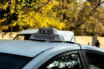 A sign with the inscription Taxi on the roof of a white car parked near the park. The concept of...