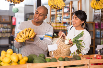 Positive hispanic couple choosing fresh foods in fruit and vegetable section of supermarket