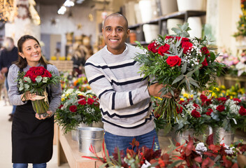 Woman owner of flower shop advising male customer before purchase of flowers