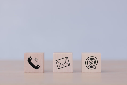 E-mail address, telephone number, and letter icons print screen on the cubic wooden block on the table for webpage business contact and customer service concept. © THAWEERAT