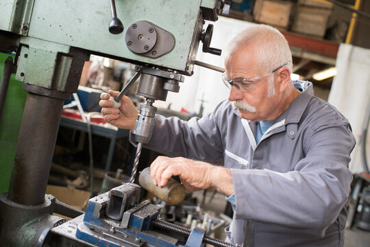 senior metal worker using industrial drilling machine in workshop