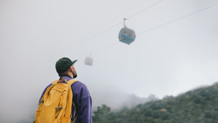 Man with a backpack stands on top of a mountain next to the funicular.