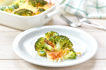 Casserole broccoli with cheese and cream sauce in a bowl on a white wooden table.