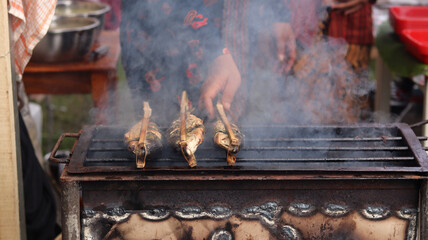 a man who is grilling fish traditionally uses a grill to sell and see the smoke. 