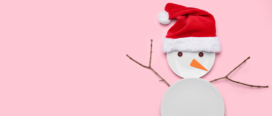 Funny snowman made of plates an Santa hat on pink background with space for text