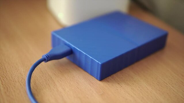 External hard drive connected to laptop laying on a table. Indicator light blinking fast. 