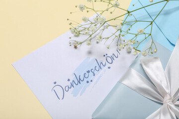 Card with text DANKE SCHON, envelope, flowers and gift box on beige background