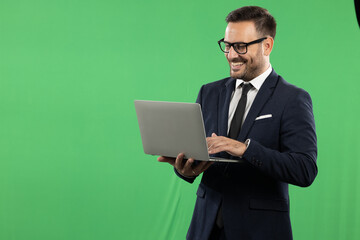 Studio portrait of business man using and holding laptop. Portrait taken on green screen, suitable for editing. Green background
