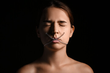 Young woman with chain on mouth against dark background. Censorship concept
