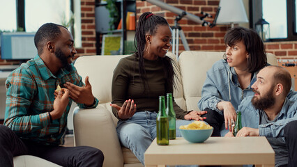 Diverse people laughing together and drinking beer, having fun and bonding at social gathering. Cheerful friends enjoying chill conversation and chatting about memories. Handheld shot.