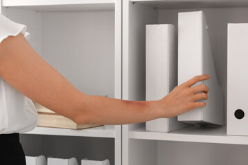 Young woman with bruised arm taking folder from shelf in office, closeup