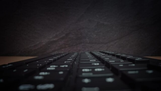 Bright white letters and numerals on buttons of black keyboard standing on desktop in office room against black wall macro