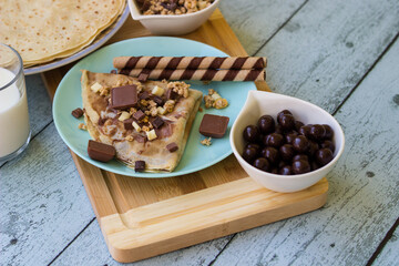 Crepes with chocolate on cutting board with ingredients. Rustic wooden background