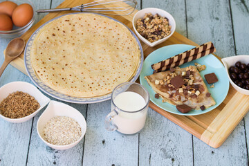 Crepes with chocolate on cutting board with ingredients. Rustic wooden background