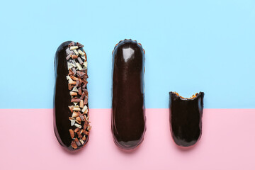 Whole and bitten chocolate eclairs on color background