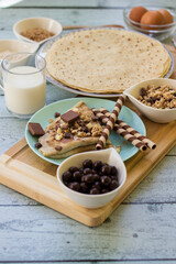 Crepes with chocolate on cutting board with ingredients. Rustic wooden background