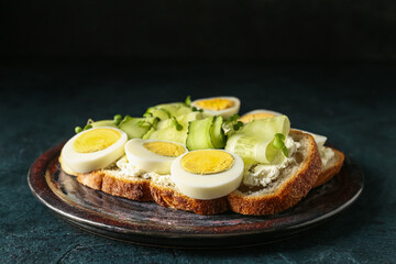 Plate of tasty toasts with boiled egg and cucumber on dark color background