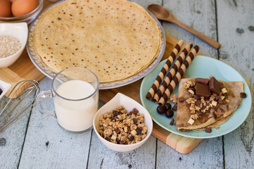 Crepes with chocolate on cutting board with ingredients. Rustic wooden background