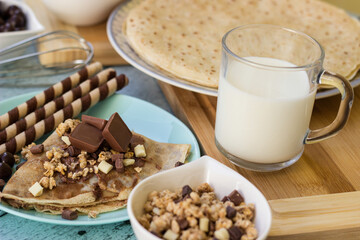 Crepes with chocolate on cutting board with ingredients. Rustic wooden background