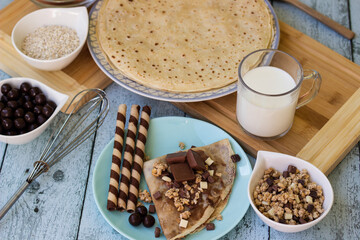 Crepes with chocolate on cutting board with ingredients. Rustic wooden background