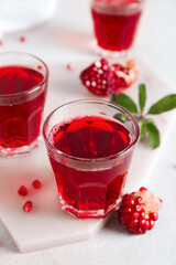 Board with glasses of tasty pomegranate juice on light background, closeup