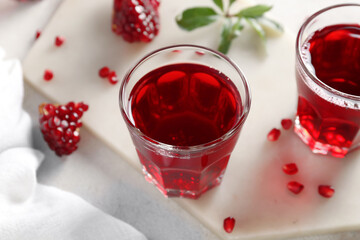 Board with glasses of tasty pomegranate juice on light background, closeup