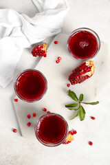 Board with glasses of fresh pomegranate juice on light background