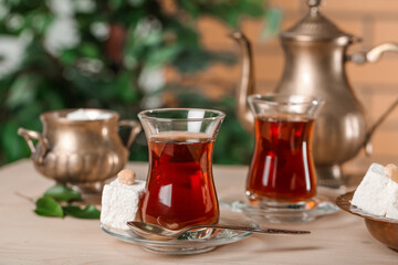 Saucer with glass of Turkish tea and dessert on table in room, closeup