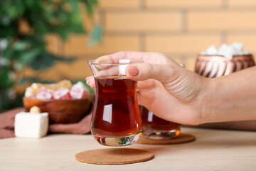 Woman with glass of Turkish tea at table in room, closeup - obrazy, fototapety, plakaty