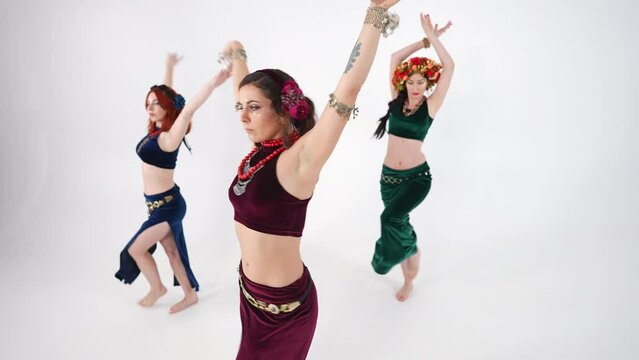 Beautiful women shaking chest and hips turning in slow motion dancing Middle Eastern dance. Serious confident graceful slim Caucasian belly dancers at white background