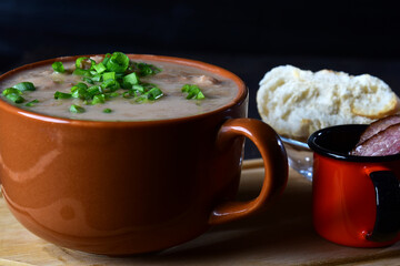 bean broth with chives, bacon and bread, served in an earthenware cup on a wooden base