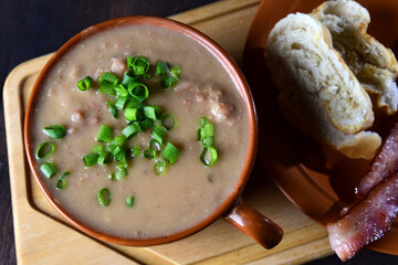 bean broth with chives, bacon and bread, served in an earthenware cup on a wooden base