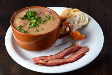 bean broth with chives, bacon and bread, served in an earthenware cup on a wooden base
