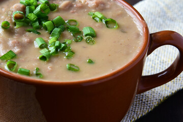 bean broth with chives, bacon and bread, served in an earthenware cup on a wooden base