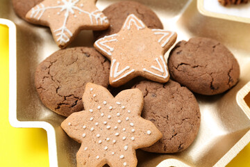 Plate in shape of Christmas tree with cookies on yellow background, closeup