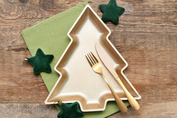 Plate in shape of Christmas tree with cutlery, stars and napkin on wooden background