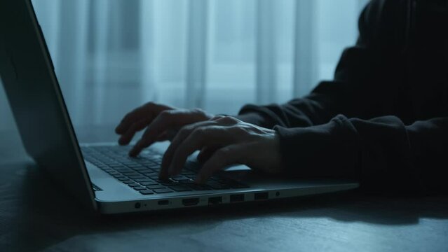 Silhouette of a computer hacker in a hood sitting at a laptop. Cyber attack.