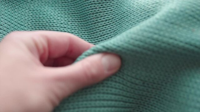 Male hand touching soft and cozy green acrylic knitted sweater.