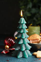 Burning Christmas tree candle with decor and treats on dark background, closeup