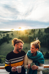 Fototapeta premium Young couple drinking coffee or tea while standing on their balcony at sunrise