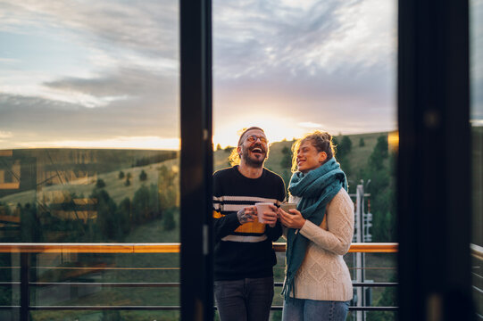 Young couple drinking coffee or tea while standing on their balcony at sunrise